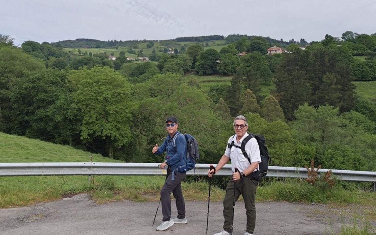 Dos peregrinos con bastones sobre una colina verde del Camino